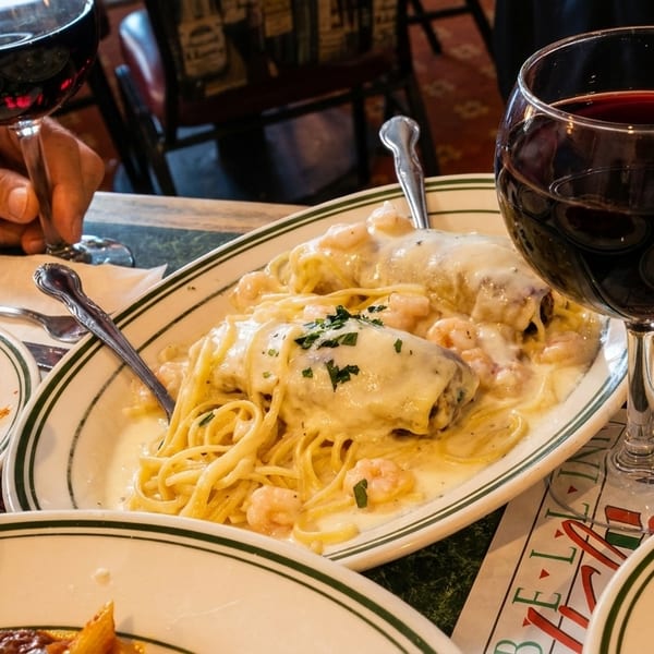 A table set with Italian pasta dishes, red wine, and a person's hand holding a wine glass.