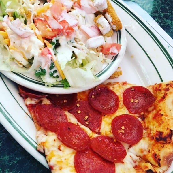 Pepperoni pizza with melted cheese and a creamy chicken salad on a white plate.