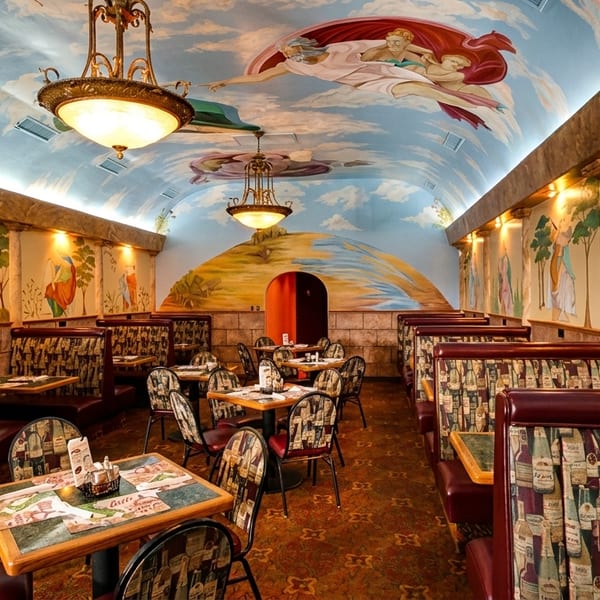 Restaurant interior with Renaissance-style murals on walls and ceiling, featuring booths and tables.