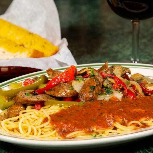Spaghetti with sausage, peppers, onions, and red sauce, served with garlic bread and wine.