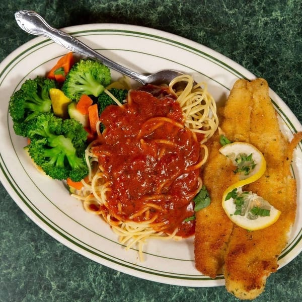 Fried fish with lemon, spaghetti with red sauce, and steamed vegetables on a white plate.