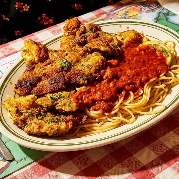 Chicken parmesan with spaghetti and red sauce on a red and white checkered tablecloth.