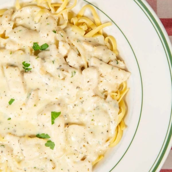 Creamy chicken alfredo pasta with parsley flakes in a white bowl with a green rim.