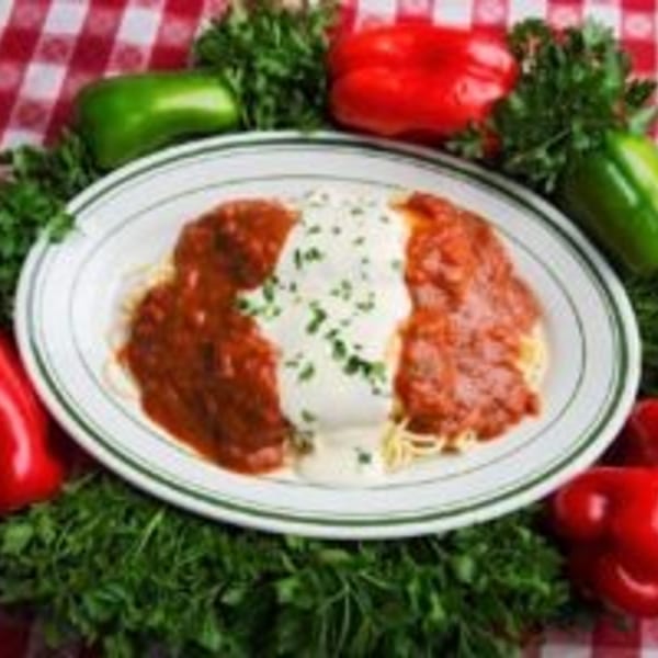 Plate of two red-sauce-covered entrée portions garnished with herbs, surrounded by bell peppers and parsley on a checkered tablecloth.