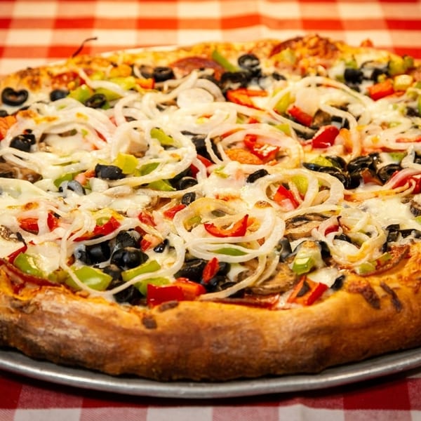 A whole supreme pizza with onions, peppers, olives, and mushrooms on a red and white checkered tablecloth.