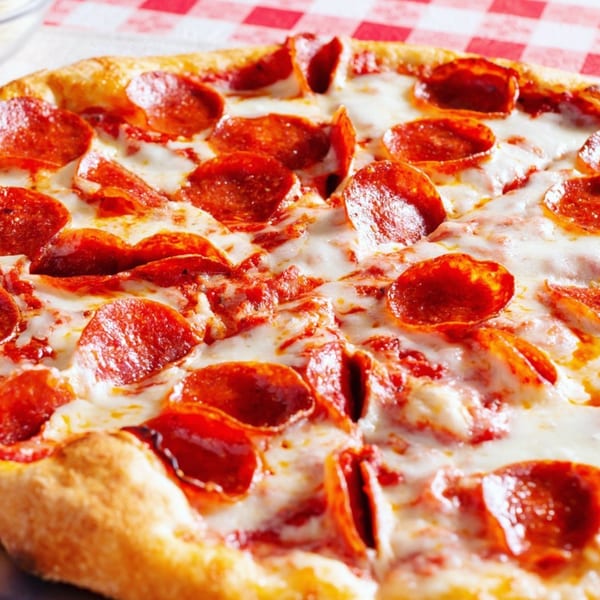Close-up of a pepperoni pizza with melted cheese and golden crust on a red-and-white checkered tablecloth.