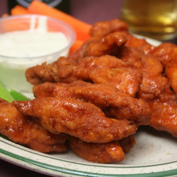 Crispy sauced chicken wings piled on a plate with creamy dipping sauce and celery.