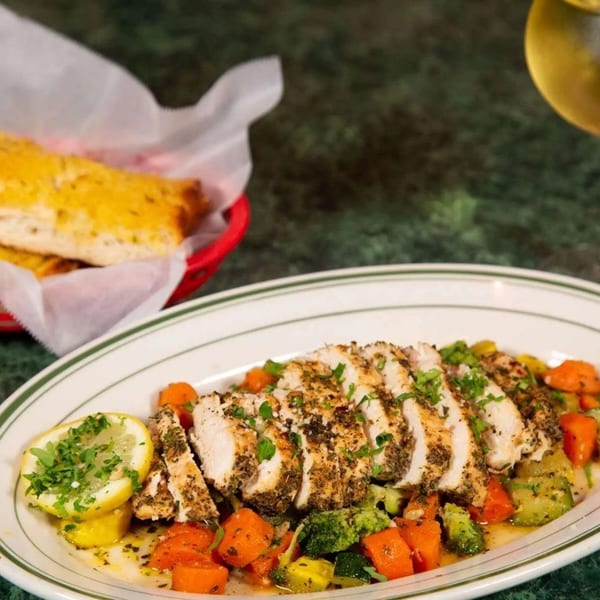 Sliced chicken breast with roasted vegetables, garlic bread, and a glass of white wine.