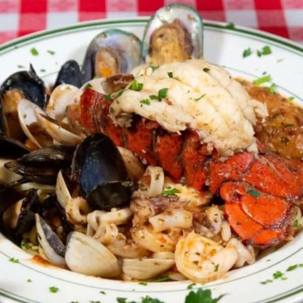 Platter of mussels, clams, shrimp, lobster, and fish topped with herbs and creamy sauce on a checkered tablecloth
