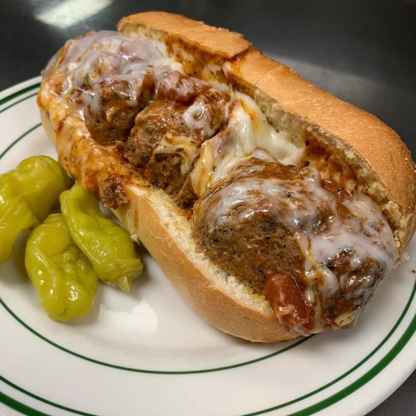 Cheesy meatball sub with marinara sauce on a toasted roll, served with pepperoncini peppers on a white plate.