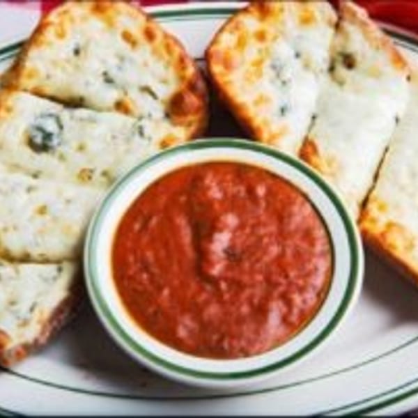 Crispy cheesy garlic bread slices arranged around a bowl of marinara sauce on a white plate.