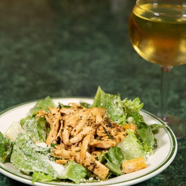 Chicken Caesar salad with parmesan cheese and a glass of white wine on a green table.