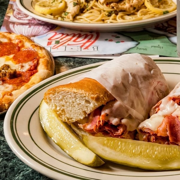A pepperoni and sausage pizza, a sub sandwich with pickles, and pasta with lemon slices.