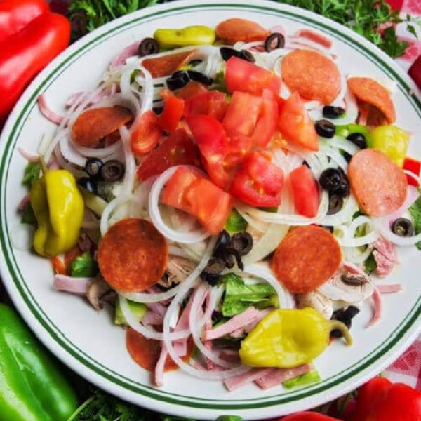 Antipasto salad topped with tomatoes, pepperoni, onions, black olives, banana peppers, and mixed greens.