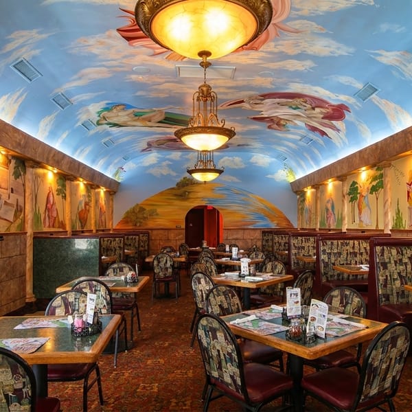 Restaurant interior with a vaulted ceiling painted with clouds and figures, and murals on the walls.