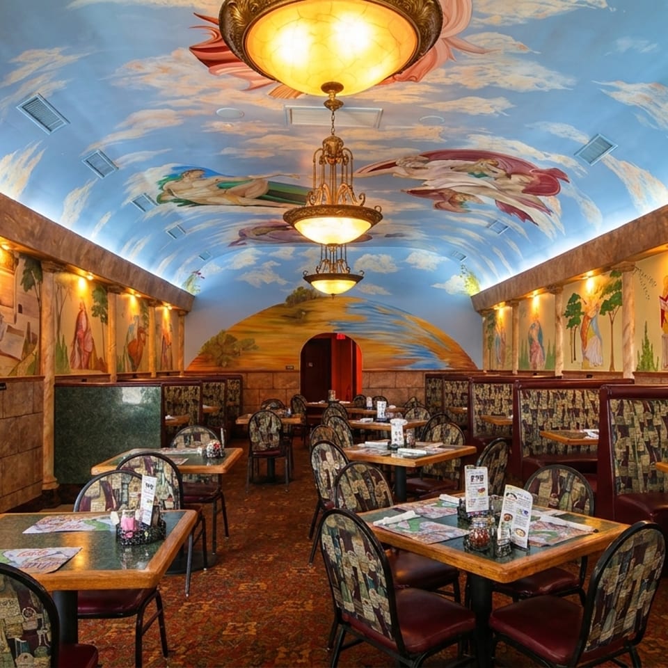 Restaurant interior with a vaulted ceiling painted with clouds and figures, and murals on the walls.