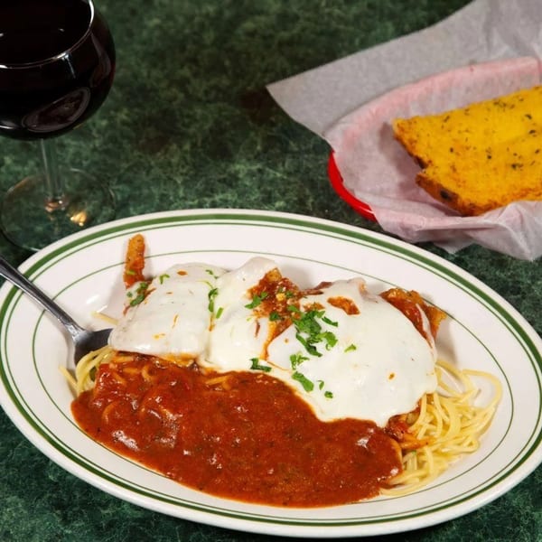 Chicken parmesan with spaghetti, red sauce, melted cheese, parsley, garlic bread, and red wine.