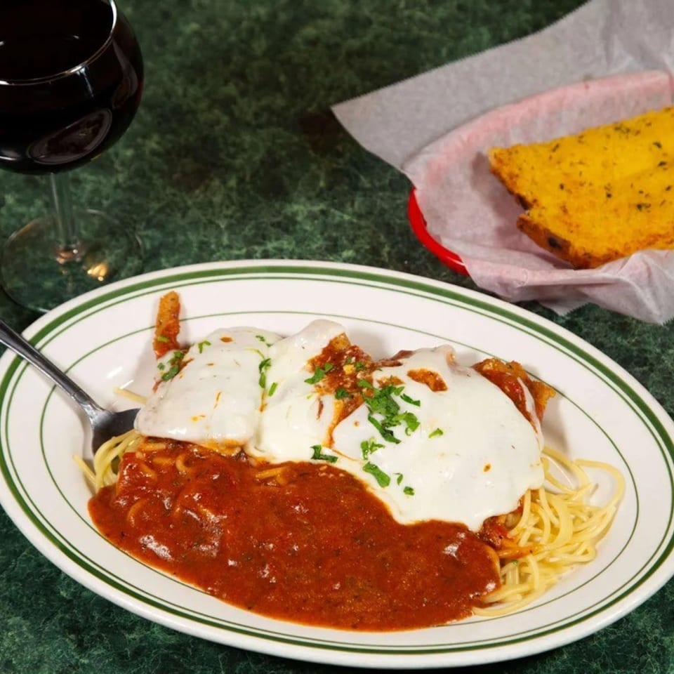 Chicken parmesan with spaghetti, red sauce, melted cheese, parsley, garlic bread, and red wine.