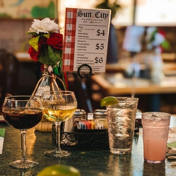 A Sun City Happy Hour menu with drinks, including wine and cocktails, on a restaurant table.