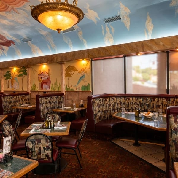 A vibrant Italian restaurant interior with painted murals, ornate chandeliers, and patterned booth seating.