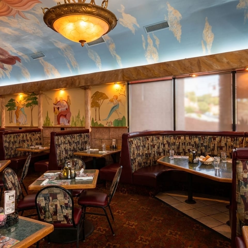 A vibrant Italian restaurant interior with painted murals, ornate chandeliers, and patterned booth seating.