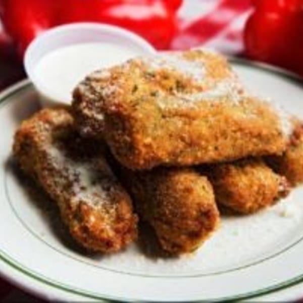 Plate of golden-brown breaded fried food surrounded by red tomatoes on a red-and-white checkered tablecloth.