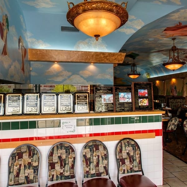 Restaurant interior with a sky-painted ceiling, murals, awards, and a counter with bar stools.
