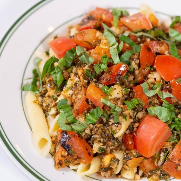 Penne pasta topped with roasted tomatoes, herbs, and crumbled cheese on a white plate.