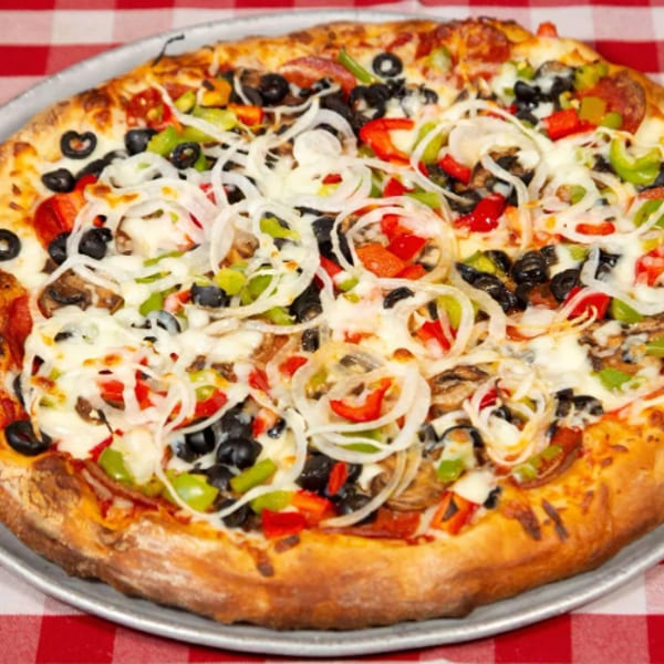 Loaded vegetarian pizza with black olives, onions, peppers, mushrooms, tomatoes, and melted cheese on a metal tray.