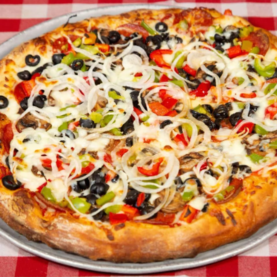 Loaded vegetarian pizza with black olives, onions, peppers, mushrooms, tomatoes, and melted cheese on a metal tray.